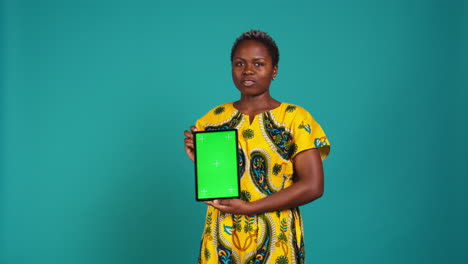 Happy-natural-girl-showing-a-green-screen-against-blue-background