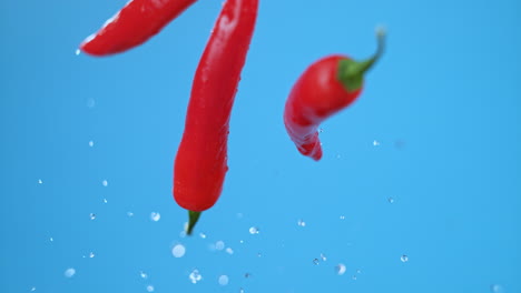 three large red chili bell peppers jumping in air with water droplets