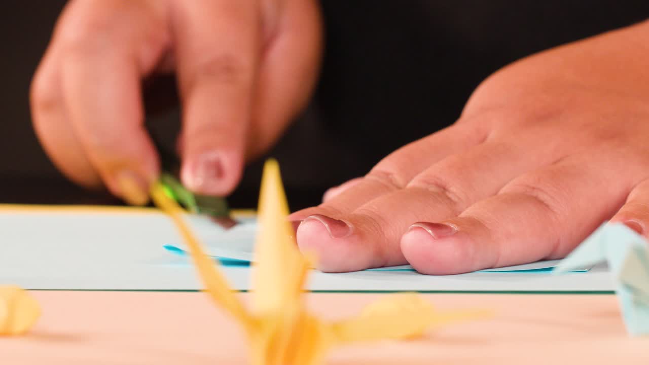Close up shot of hands carefully folding blue paper into origami with soft studio lighting