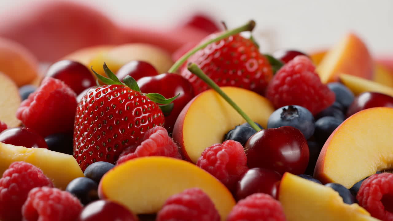 Nærbilde av blandet sommerskål med frukt, full av modne jordbær, ferskener, kirsebær, blåbær og bringebær, duggfrisk