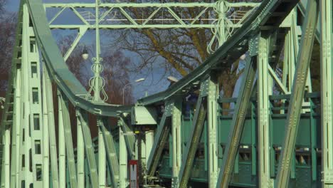 medium close-up of people and cars crossing the oskara kalpaka metal swing bridge at liepaja in sunny afternoon, medium shot