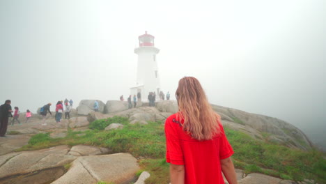 young woman walking towards lighthouse in the fog on an overcast day in nova scotia, canada