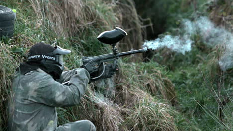 hombre escondiéndose en el suelo disparando una pistola de paintball