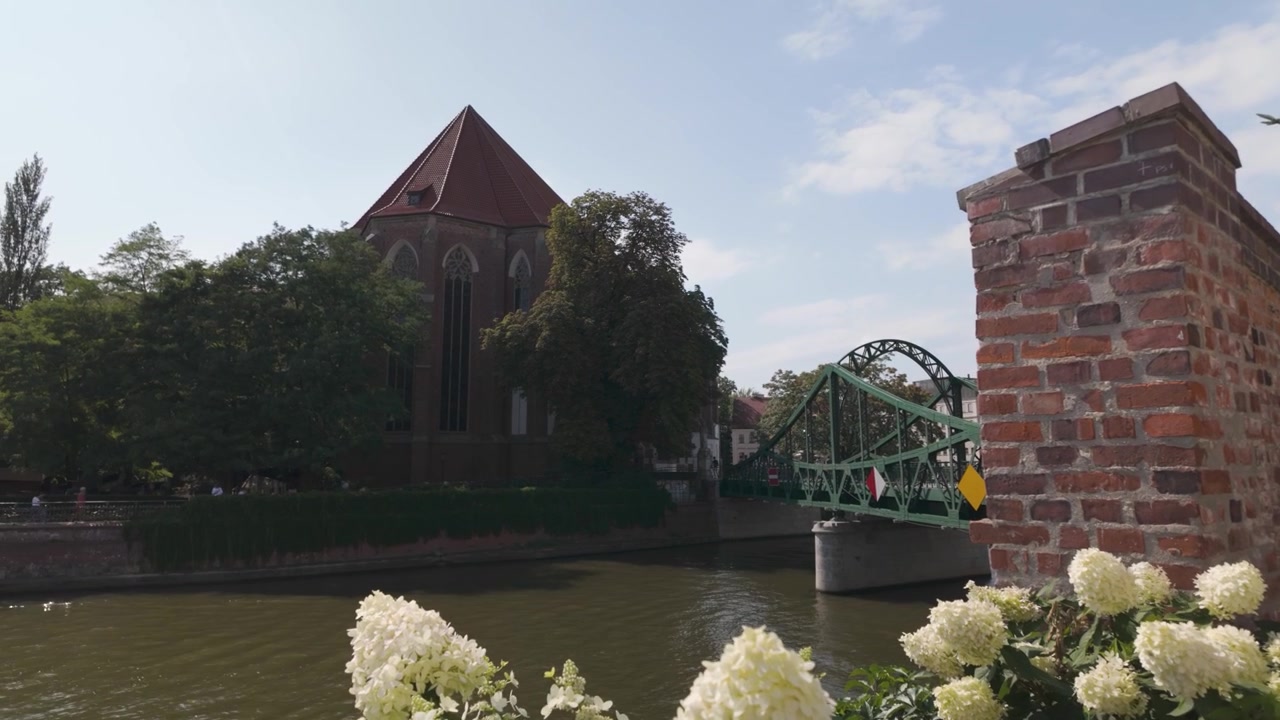 Una vista panoramica del Ponte Tumski a Breslavia, Polonia, con fiori in primo piano e una chiesa storica sullo sfondo in una giornata di sole.