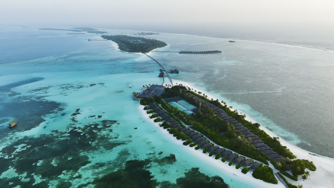 Ripresa aerea con drone che si allontana rivelando diverse bellissime isole resort tropicali collegate da ponti nell'oceano turchese limpido delle Maldive al tramonto sotto un cielo sereno