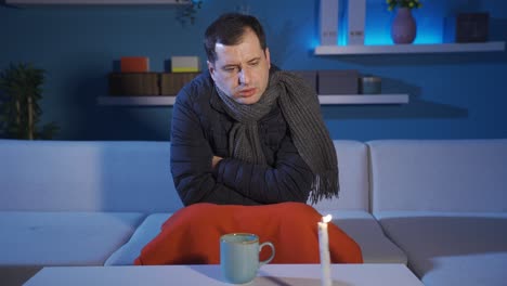 hombre solo en la casa fría bebiendo bebida caliente, sentado a la luz de las velas.