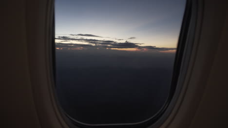 4k shot push in or dolly by a passenger from the inside of a commercial plane window to see a beautiful colorful sky after sunset.