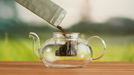 pouring loose leaf tea into a glass teapot