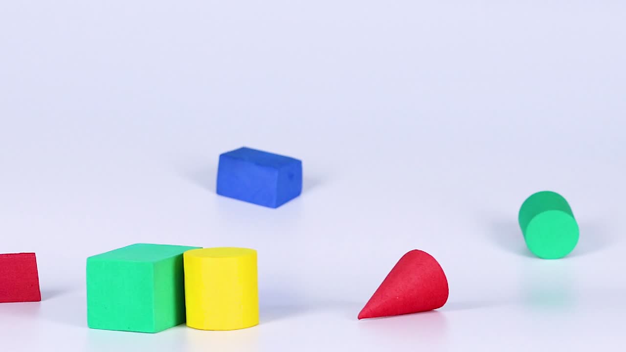 Vibrant geometric shapes tumble and interact dynamically on a white surface.