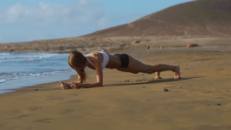 Vista-Lateral-De-Una-Hermosa-Mujer-Deportiva-En-Posición-De-Tabla-En-La-Playa-Durante-El-Atardecer.