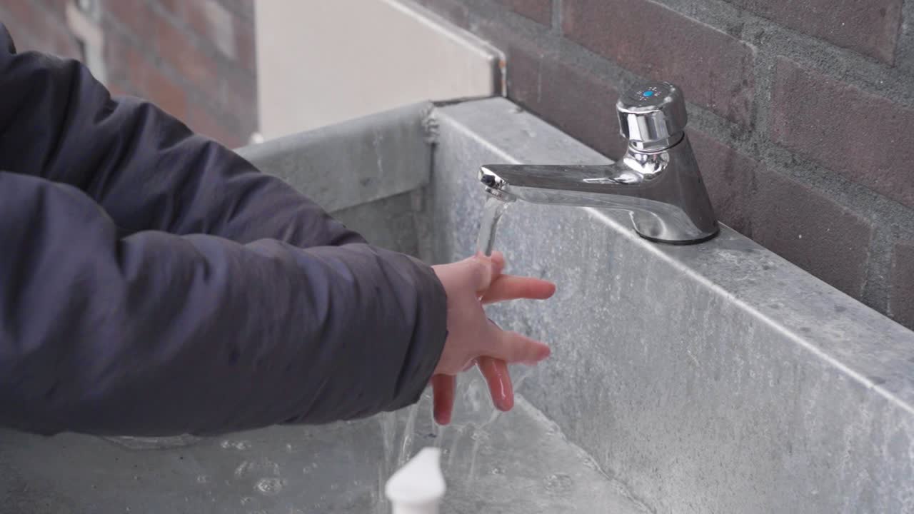 el niño se lava las manos afuera con agua fría - precauciones covid-19