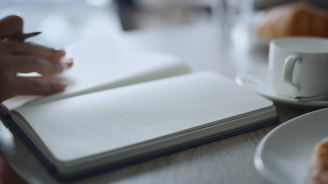 Woman hand taking notes writing pen notebook at remote workplace cafe table.