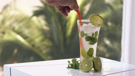 o homem agita uma bebida de mojito macia com palha de plástico numa grande mesa.