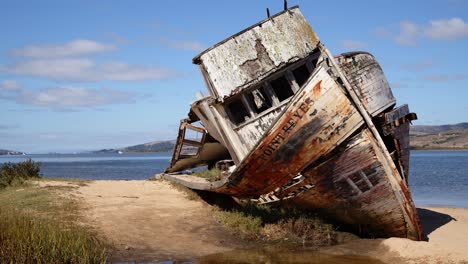 Schwenk-über-Verrottendes,-Schiffbrüchiges-Point-Reyes-Boot,-Das-An-Einem-Sonnigen-Ufer-Der-Tomales-Bucht-Angespült-Wurde