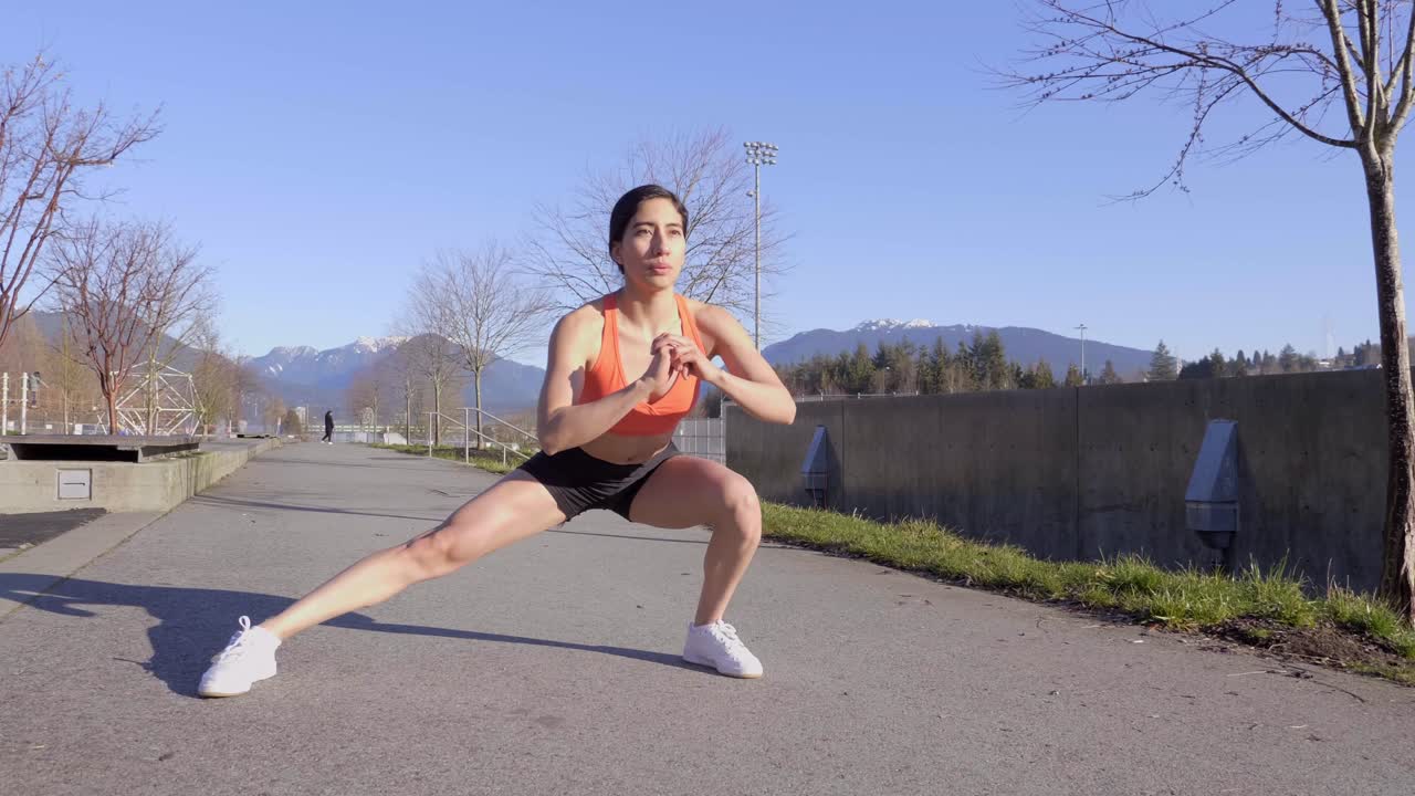 Atletisk ung kvinde træner udendørs med sidelunges.