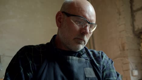 portrait of senior carpenter in protective glasses working in manufacture being concentrated and serious.