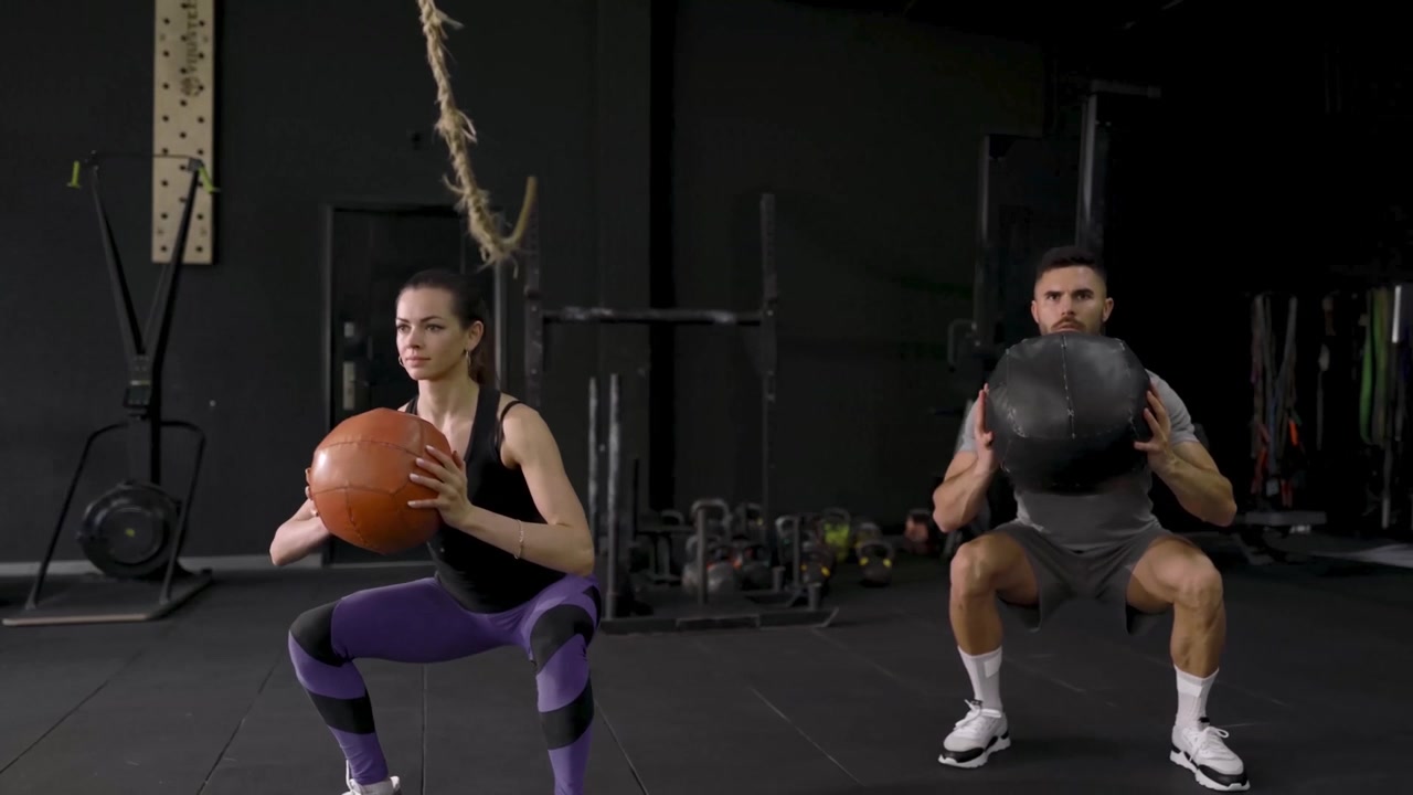 Coppia atletica che esegue squat con palla medica in una palestra buia