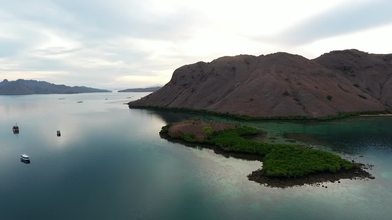 vista aérea pasando barcos y hacia las islas, en el parque nacional de komodo, tarde nublada, en indonesia - seguimiento, disparo de drones