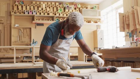 afrikaans-amerikaanse mannelijke timmerman maakt potloodmarkeringen op een houten plank in een timmerwerkplaats