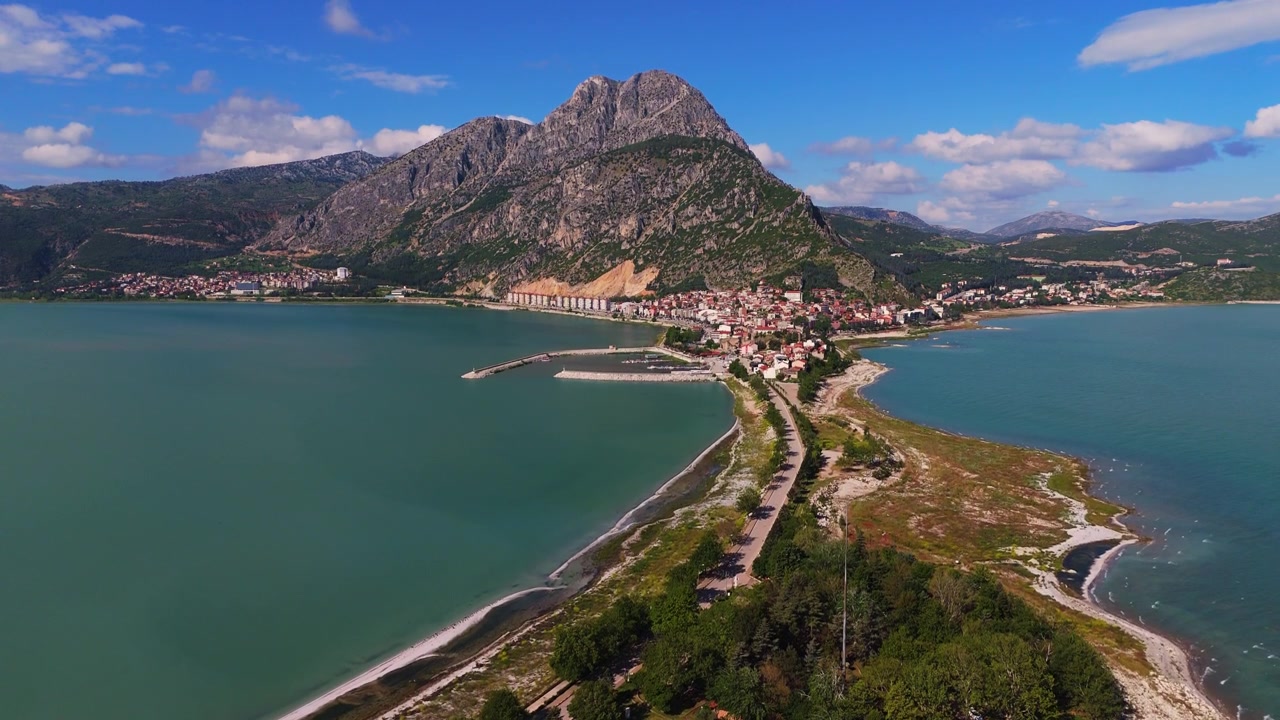 Arka planda dağlarla birlikte Eğirdir Gölü yarımadasının havadan panoramik görünümü. Türkiye'de turkuaz bir göl ve kıyı kasabası destinasyonunun etkileyici drone manzarası.