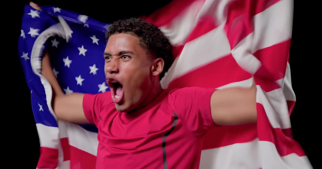 Uomo afroamericano che si sporge in avanti sorridendo, srotolando una bandiera americana con una maglietta rossa, mostrando orgoglio.