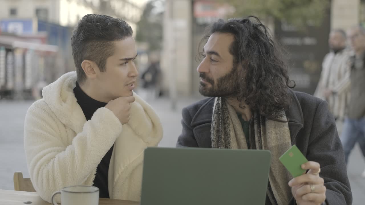 Two men having a conversation over a laptop at a cafe