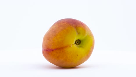 one peach fruit is rotating on the turntable isolated on the white background. close up.