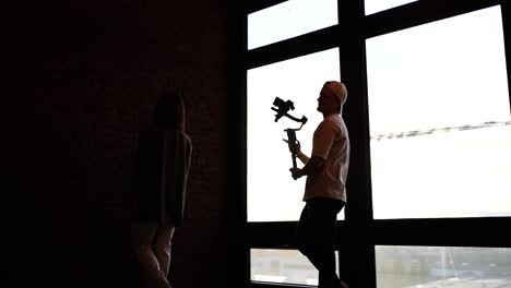 videographer with camera on gimbal film model walk near bright studio window