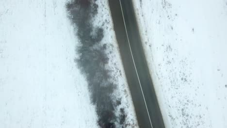birds eye view of empty road in winter, landscape covered in snow, black car driving on the road, anticipation of something to happen