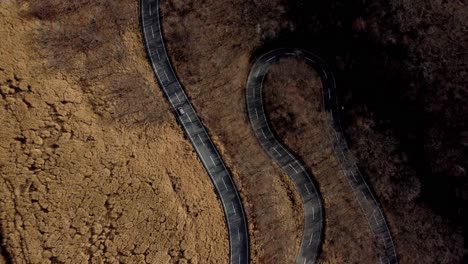 curved road slicing through barren landscape, aerial view, minimal traffic