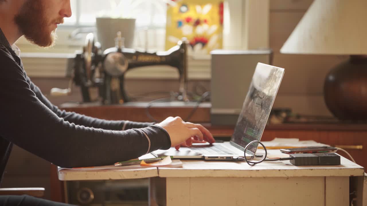 Man Browsing On The Laptop With Sewing Machine On The Background