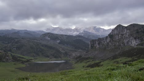 Calm-lake-surrounded-by-rocky-mountains-under-gloomy-sky