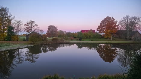 Static-shot-of-sunlight-from-the-rising-sun-falling-in-timelapse-over-a-small-lake-surrounded-by-houses-on-a-autumn-day