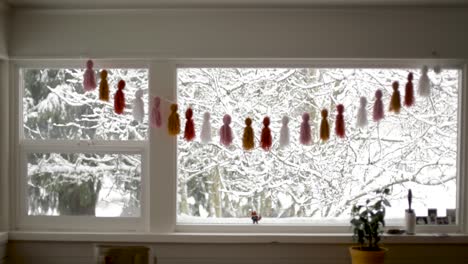 medium indoor shot of decorated window during snowy day with snow covered trees outdoors in garden