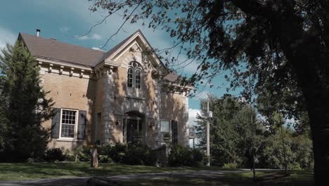 hermosa casa patrimonial de piedra revelada desde detrás de las ramas de los árboles en el resort strathmere en ottawa, canadá