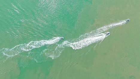 four motor boats are cutting the sea waters, leaving splashes behind them on the blue and green surface of the sea