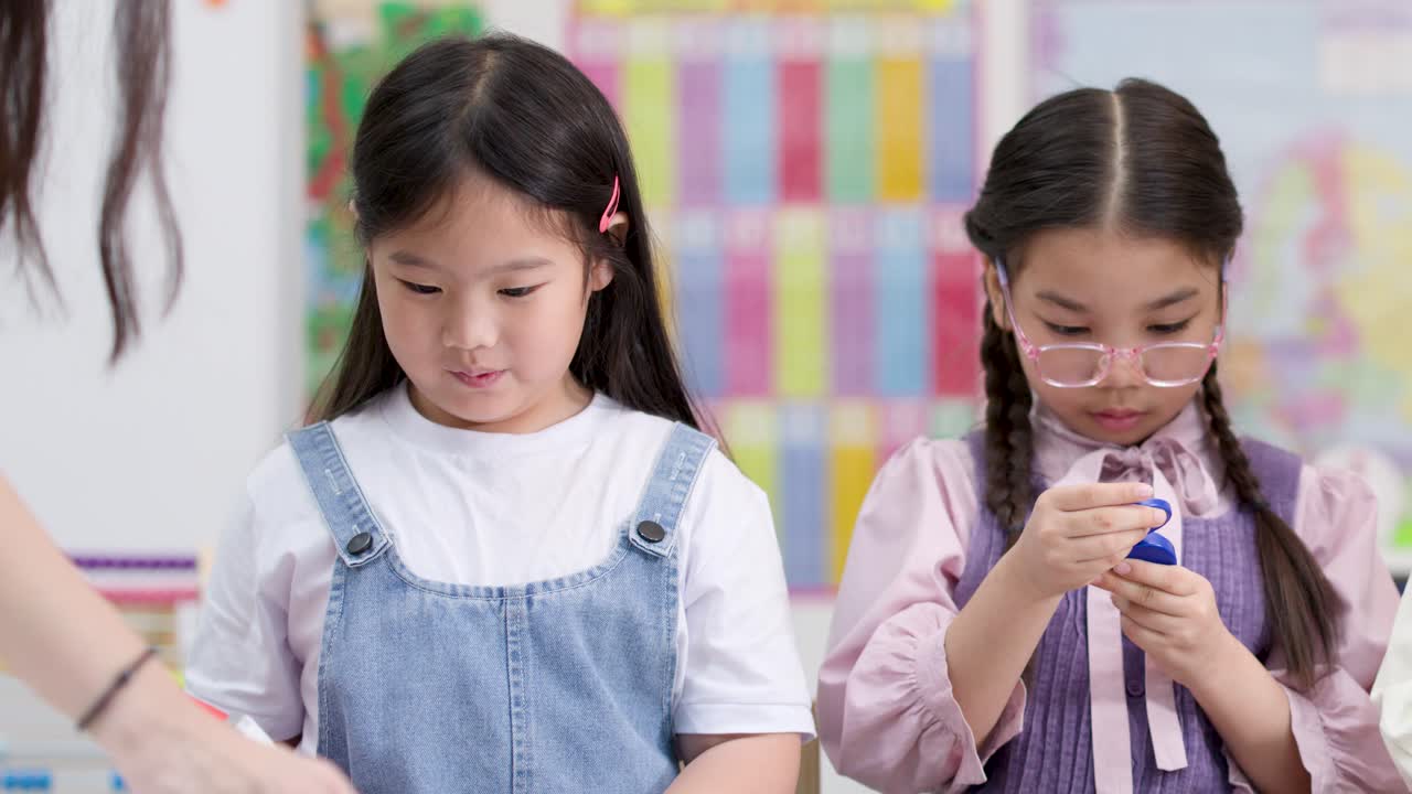 明るい教室で、小学生の女の子2人が体験型の理科の授業中にカラフルな磁石を探索しています