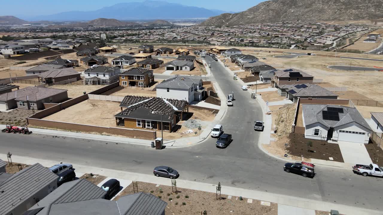 Captivating drone footage circling an under-construction house amidst a developing neighborhood, with light traffic dynamics unfolding in the foreground
