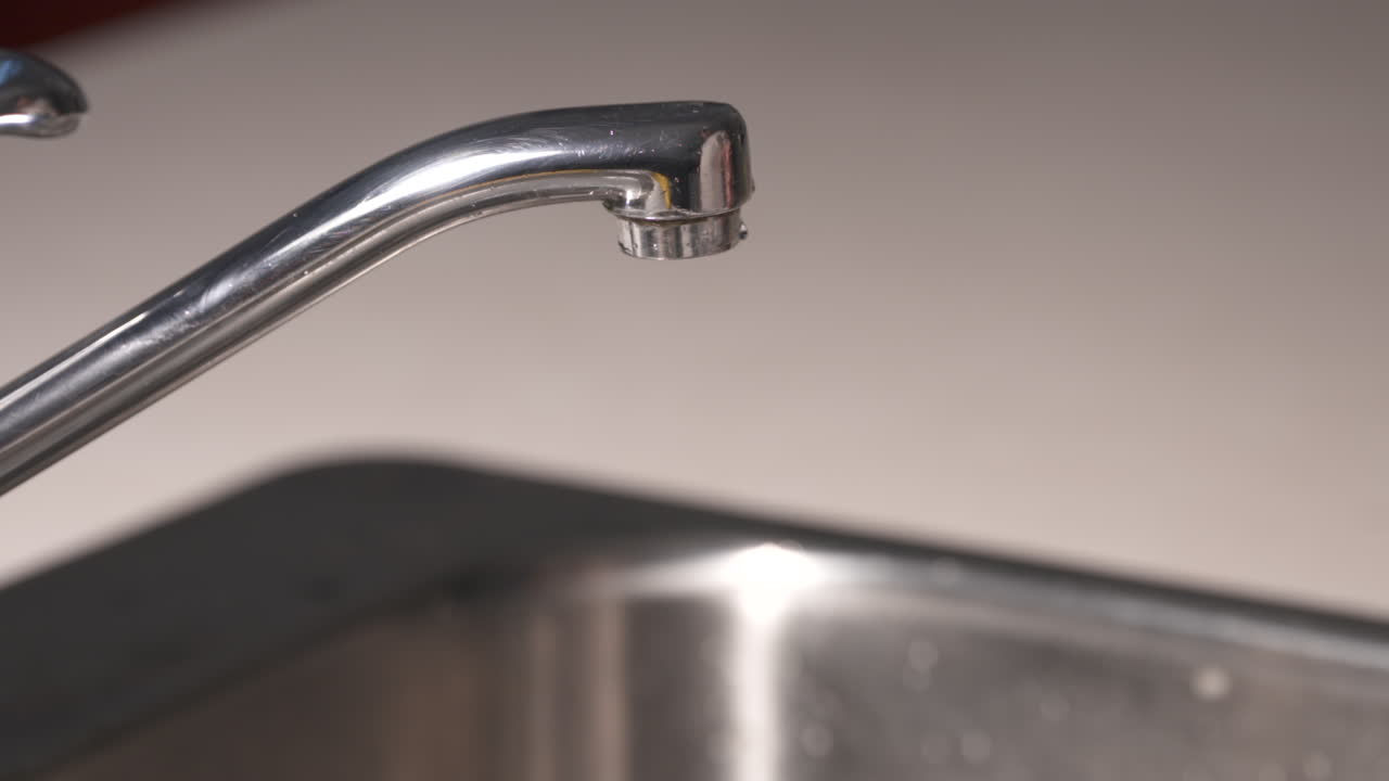 A water tap is turned on and a glass of water is filled
