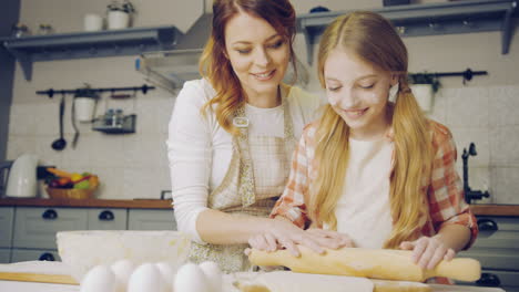 buena madre enseñando a su hija joven a cocinar y amasar una hija para galletas en la mesa de la cocina. adentro