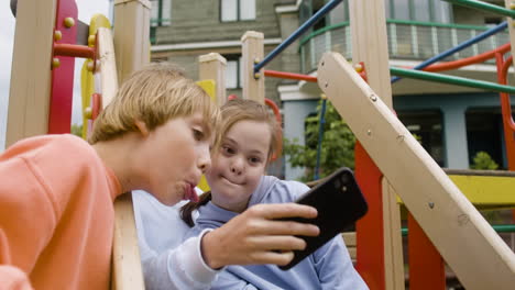 Close-up-view-of-a-little-girl-with-down-syndrome-and-her-friends-playing-with-smartphone-in-the-park-on-a-windy-day