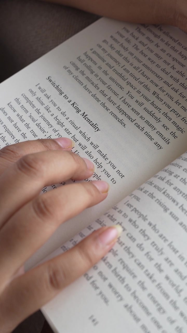 Close-up of a woman's hand gently pressing and smoothing an open book page while reading, with clearly visible printed text and soft natural window light illuminating.