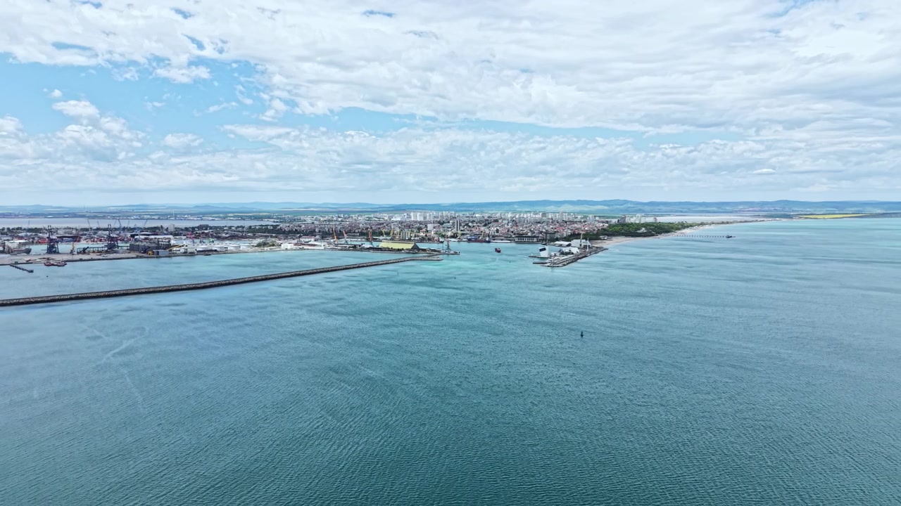 Vista de uma costa com o horizonte da cidade sob um céu nublado, mostrando barcos e atividade portuária ao longo da água