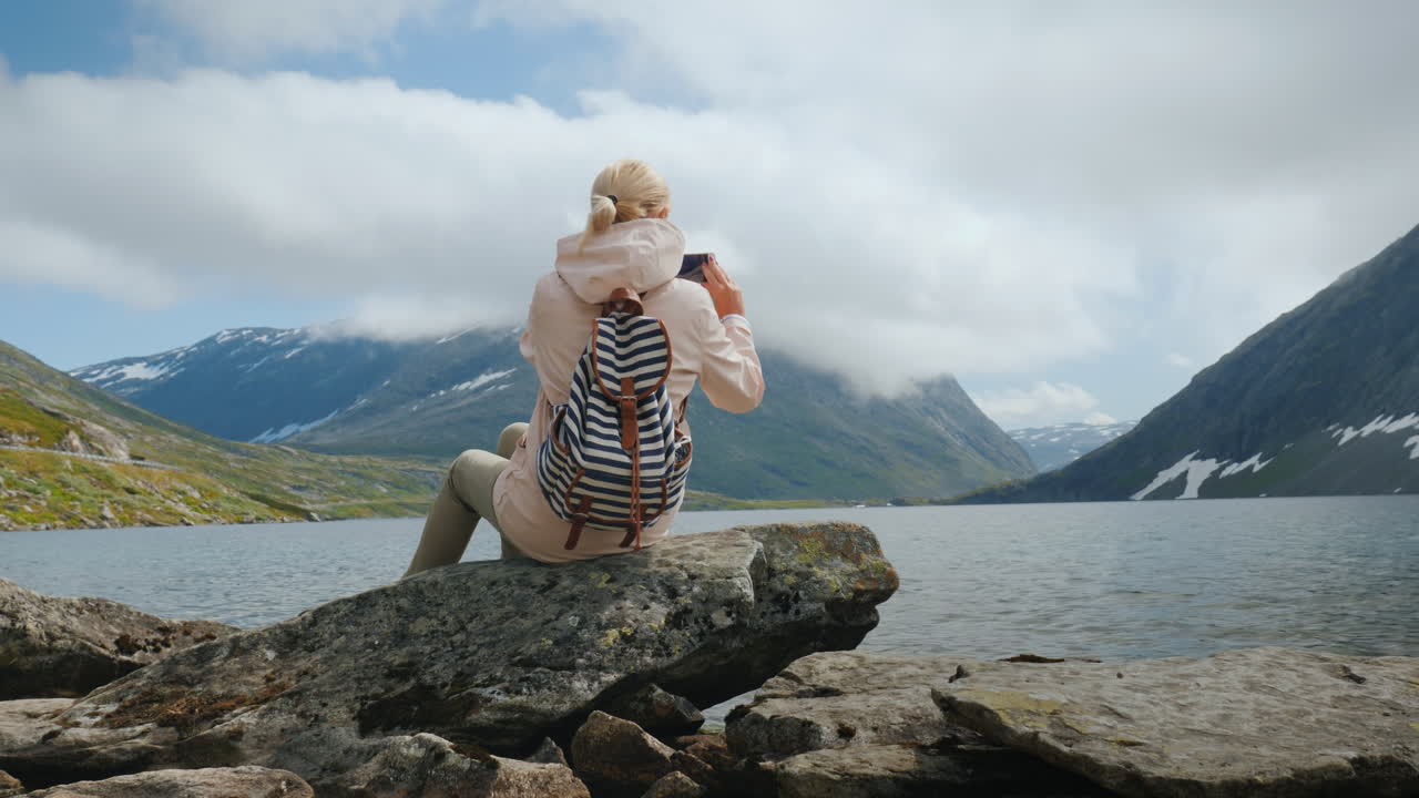 여자는 가장자리 o에서 높은 산악 노르웨이 호수 휴일의 경치를 사진을 찍는다