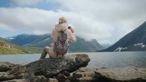 a woman takes a picture of a scenic view of a high-mountainous norwegian lake holidays at the edge o