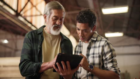 two men discussing something on a tablet in a warehouse