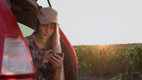 cute teenage girl sits in the trunk of a car, uses a smartphone.