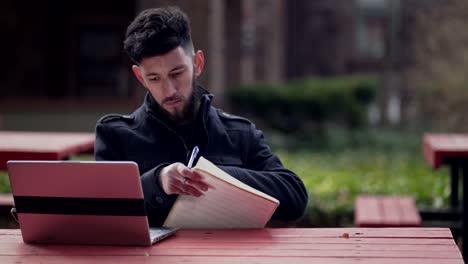 a young man copying information on his laptop and writing it on his notes - close up shot