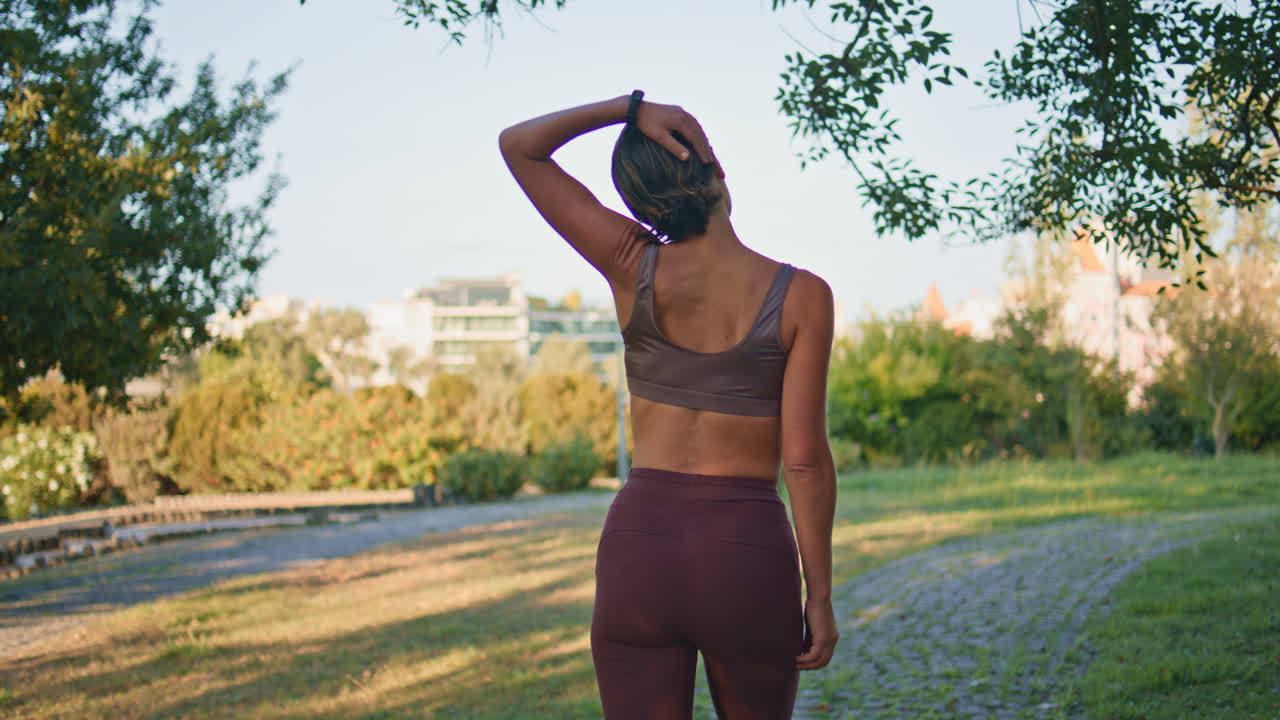 mujer de fitness estirando el cuello caminando verano vista trasera. dama calentando los músculos
