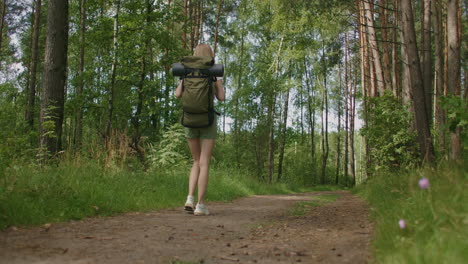 the view from the back: traveling happy caucasian woman with backpack walking on path the tropical forest